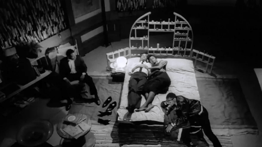 Nola Darling tumbada en su cama con uno de sus amantes y los otros dos a su alrededor